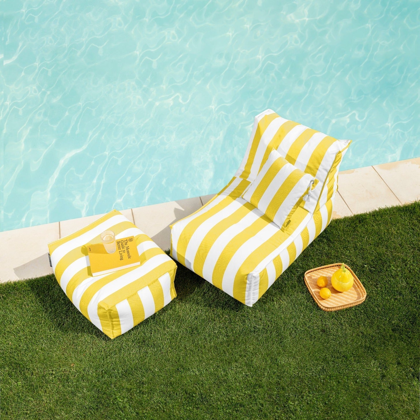 Yellow and white striped lounge chairs by a poolside with a small table and lemons.