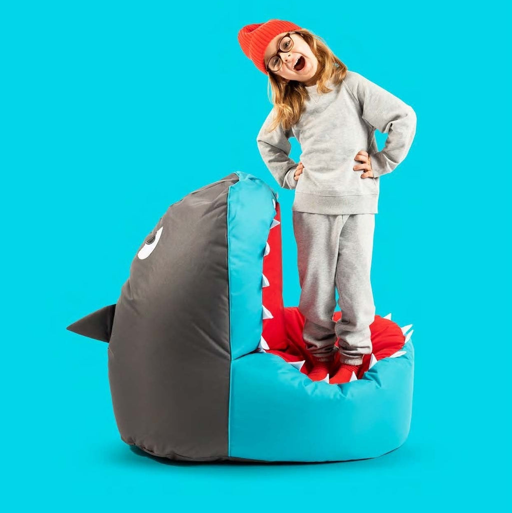 Child standing on a shark-shaped bean bag chair against a blue background