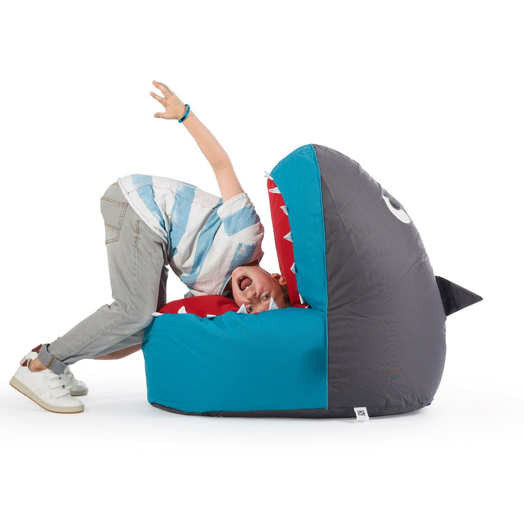 Child playing on a shark-shaped bean bag chair with blue and gray colors.