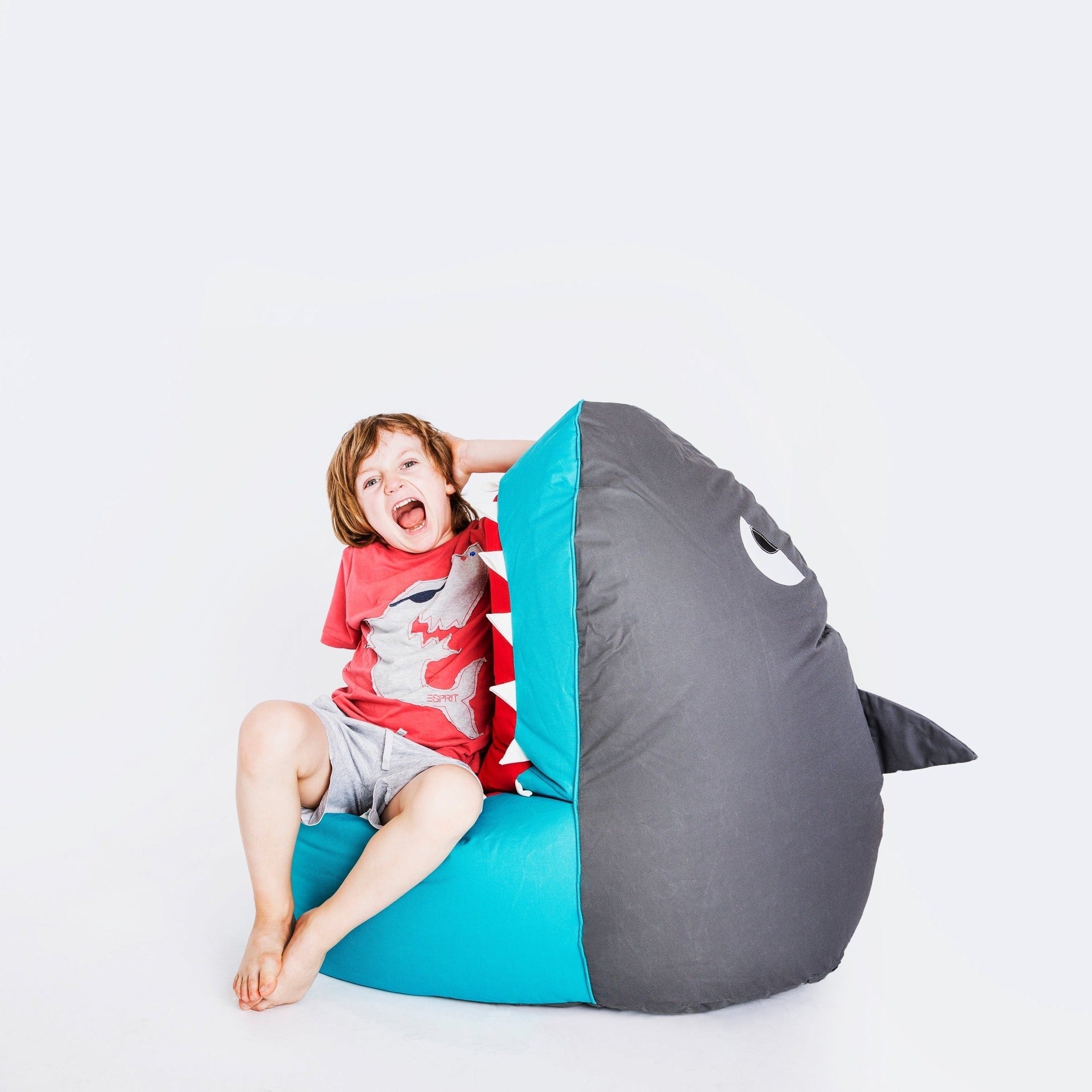 Child sitting inside a shark-shaped bean bag chair on a white background