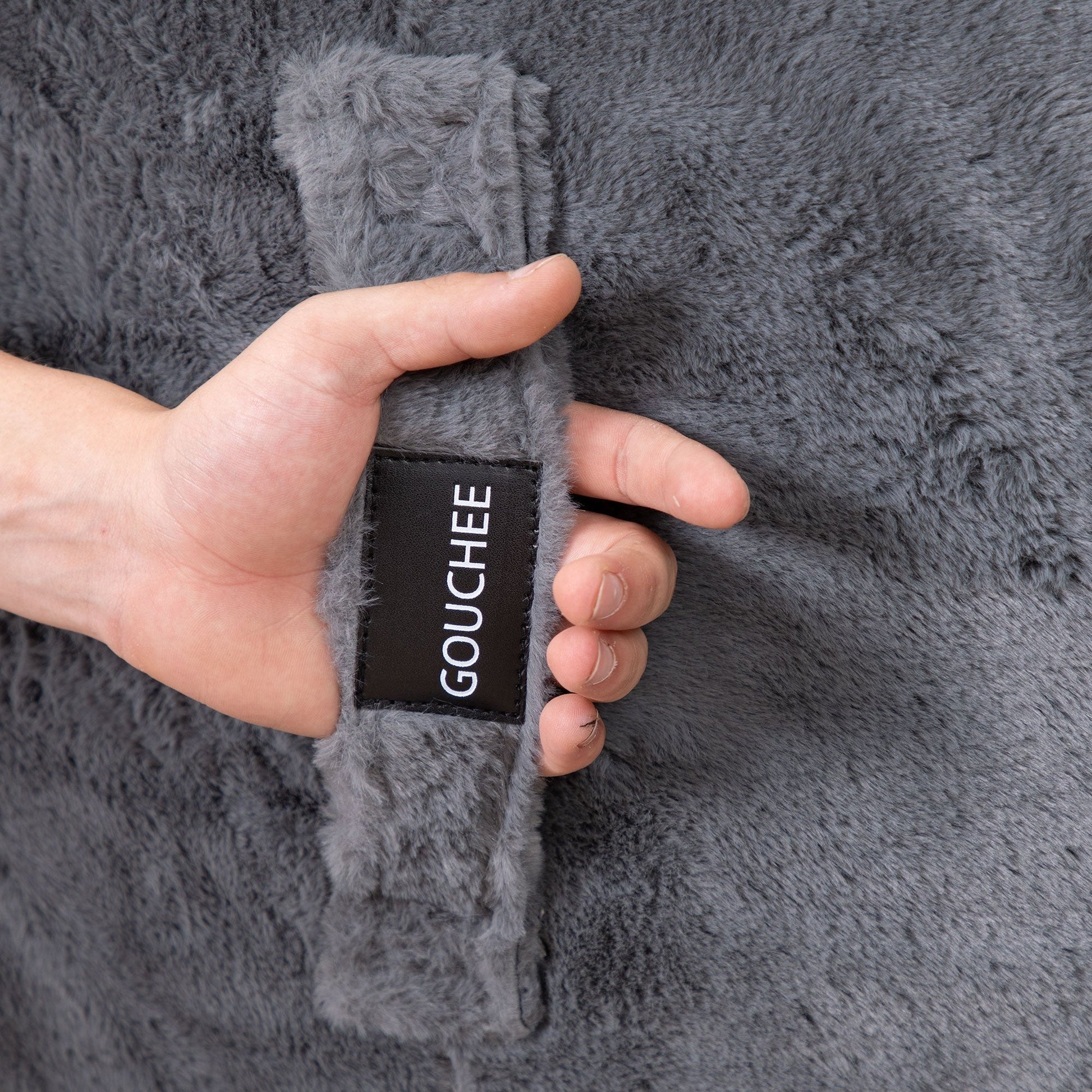 Hand holding a gray textured fabric with 'Gouchee' label