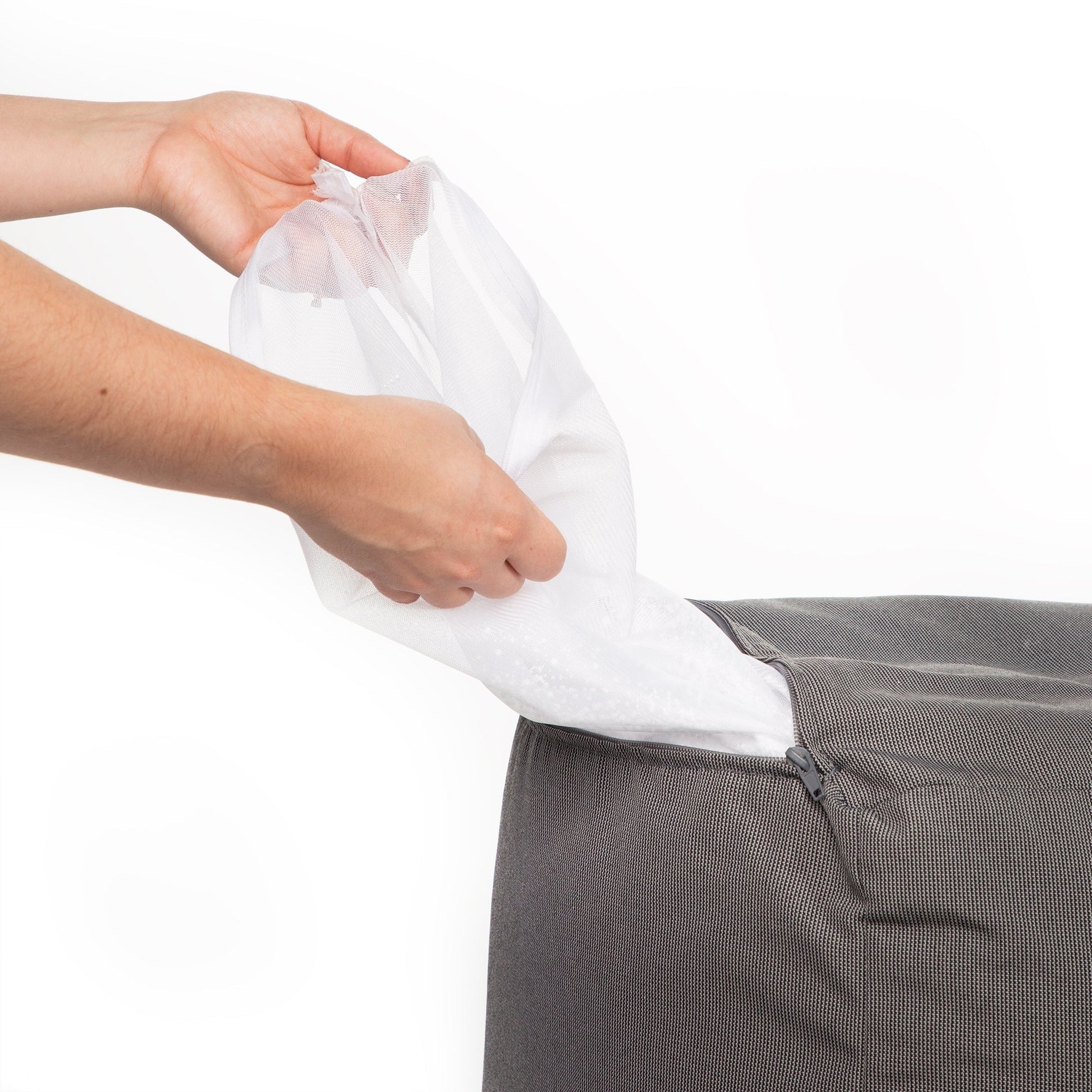Person holding a white mesh bag over a gray trash bin on a white background