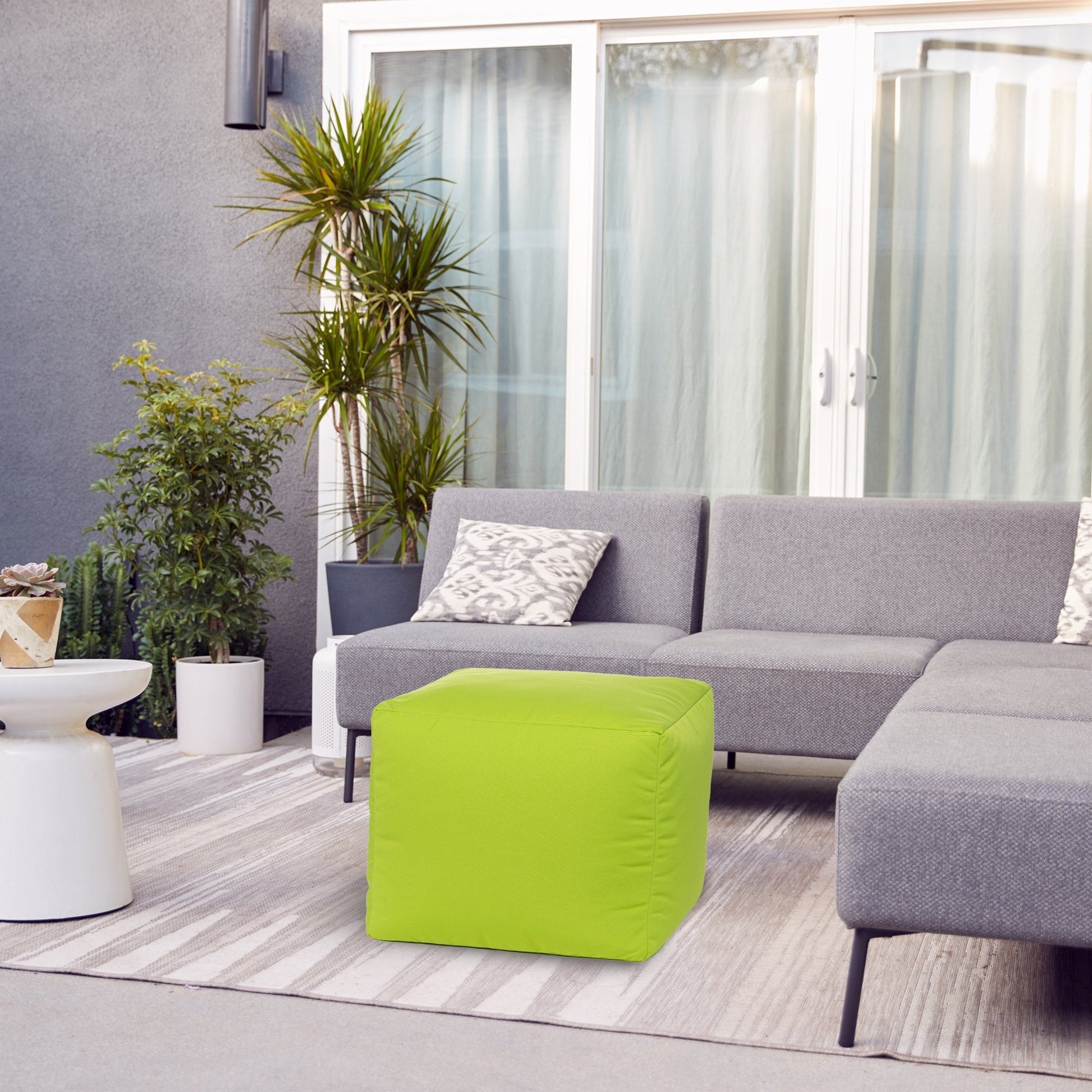 Modern living room with gray sectional sofa, green ottoman, and potted plants.
