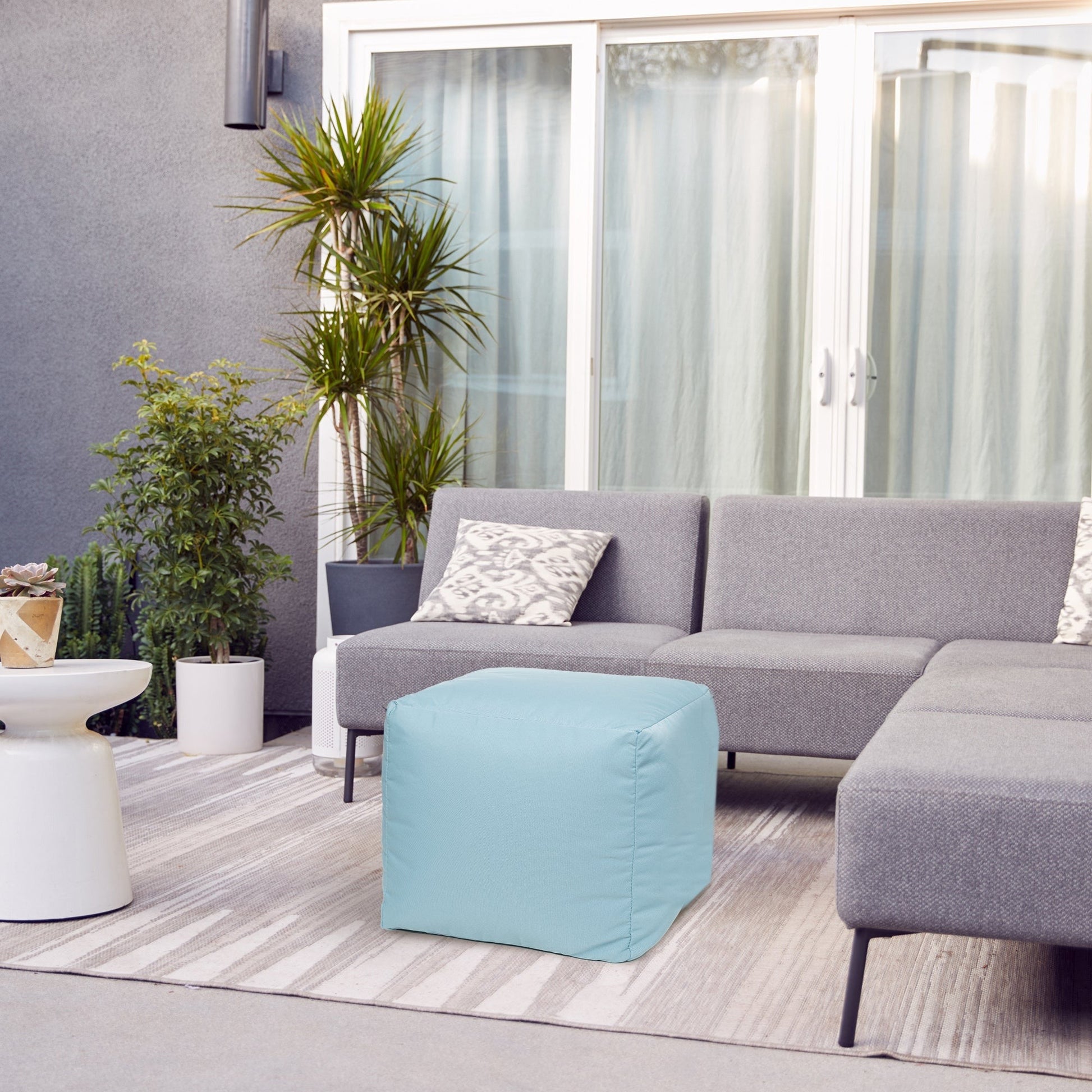 Modern living room with gray sectional sofa, light blue ottoman, and decorative plants.