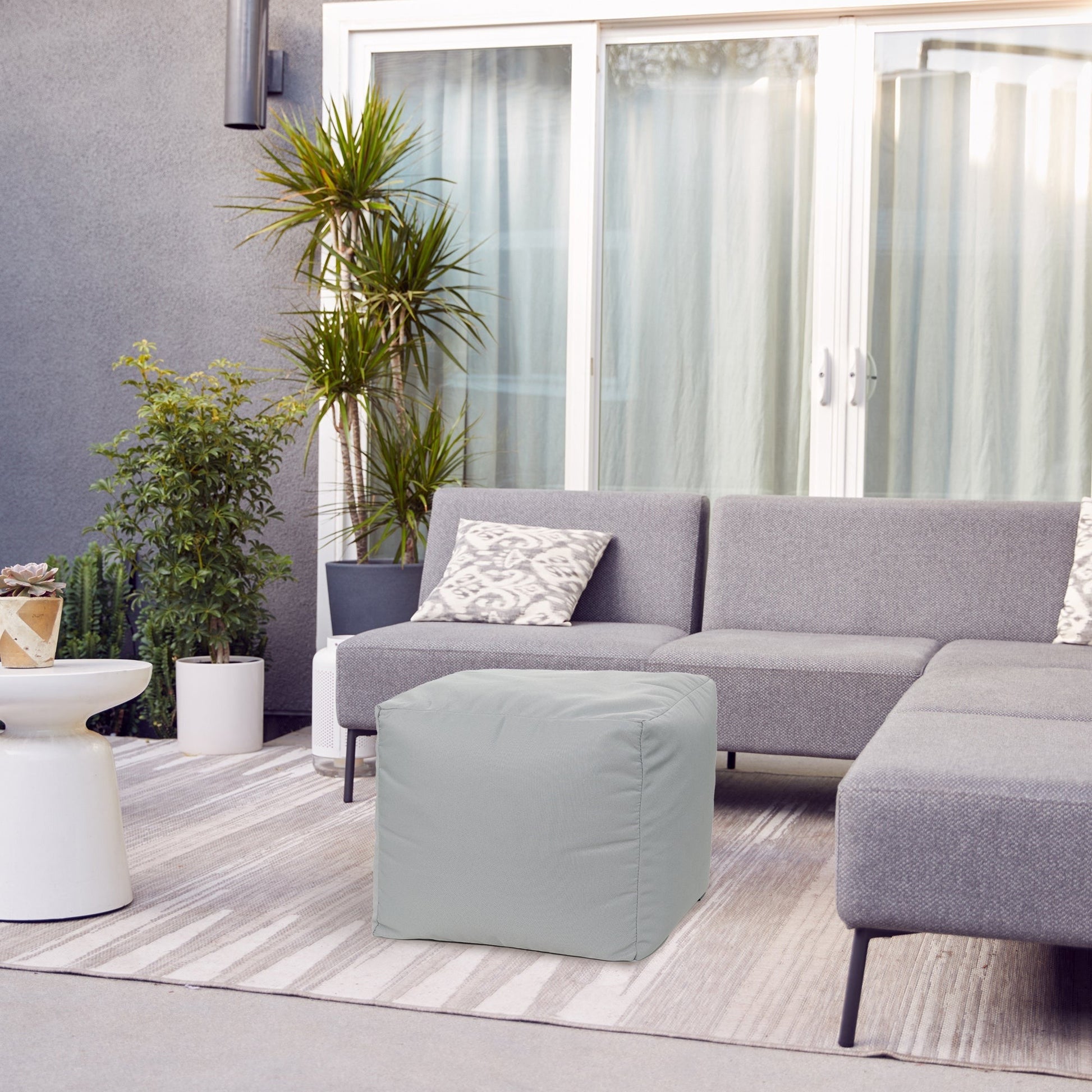 Modern living room with a gray sectional sofa, ottoman, and decorative plants.