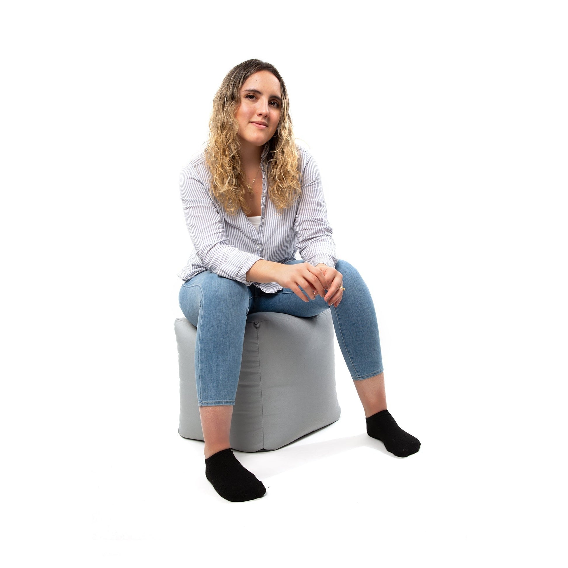 Woman sitting on a gray bean bag chair against a white background