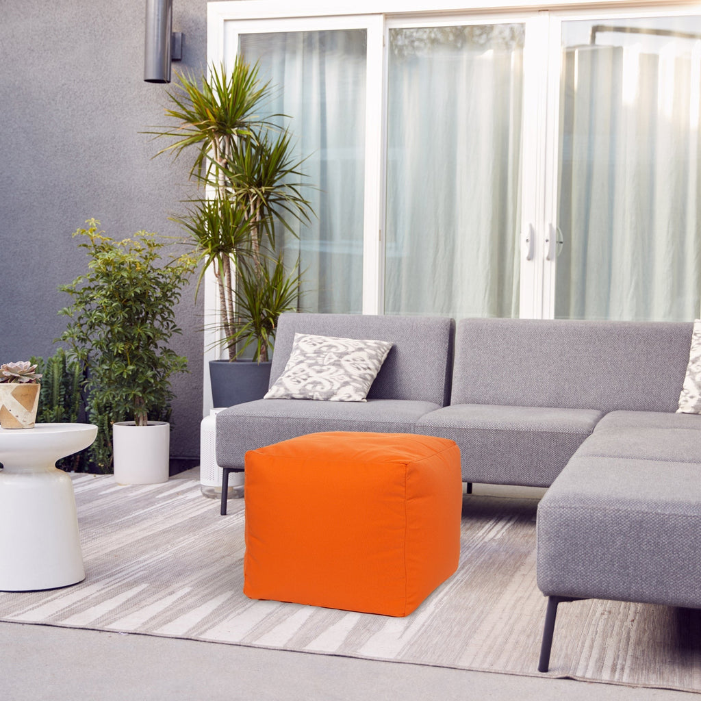 Gray sectional sofa with an orange pouf and plants in a modern living room.