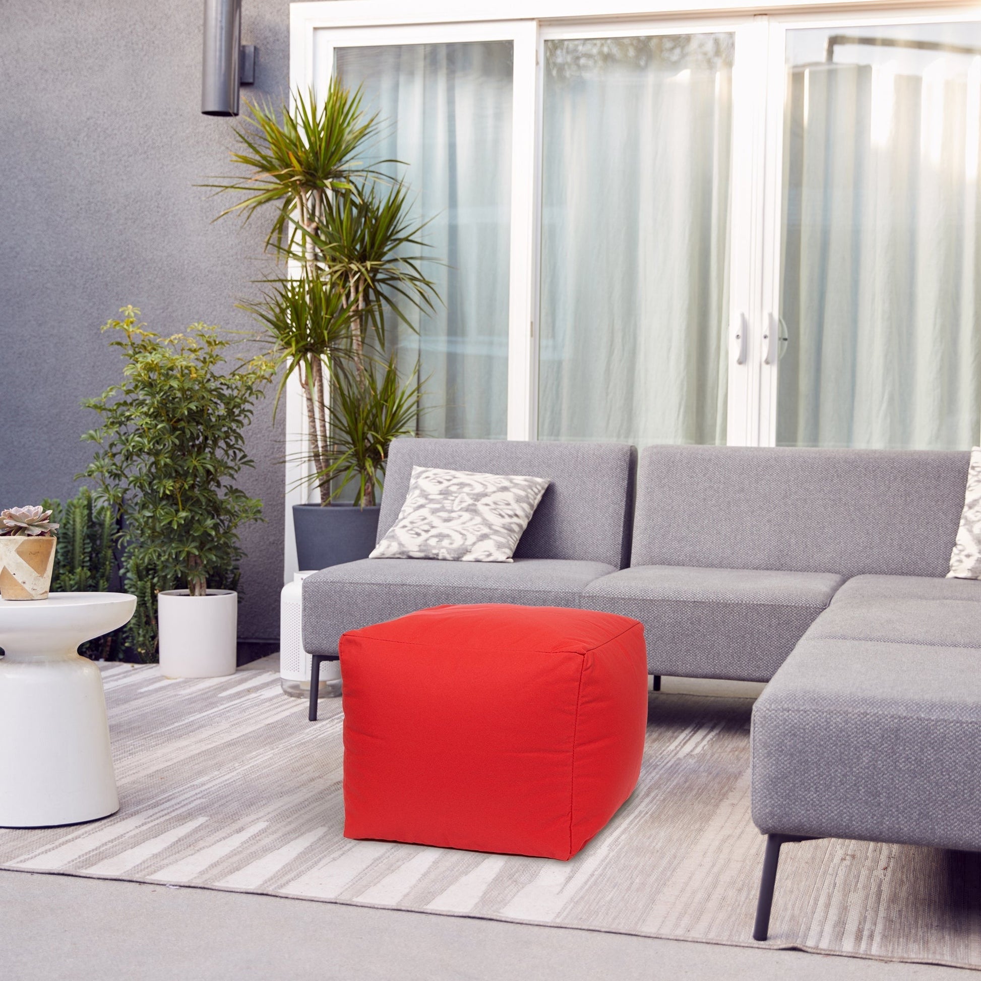 Gray sectional sofa with a red pouf in a modern living room setting.