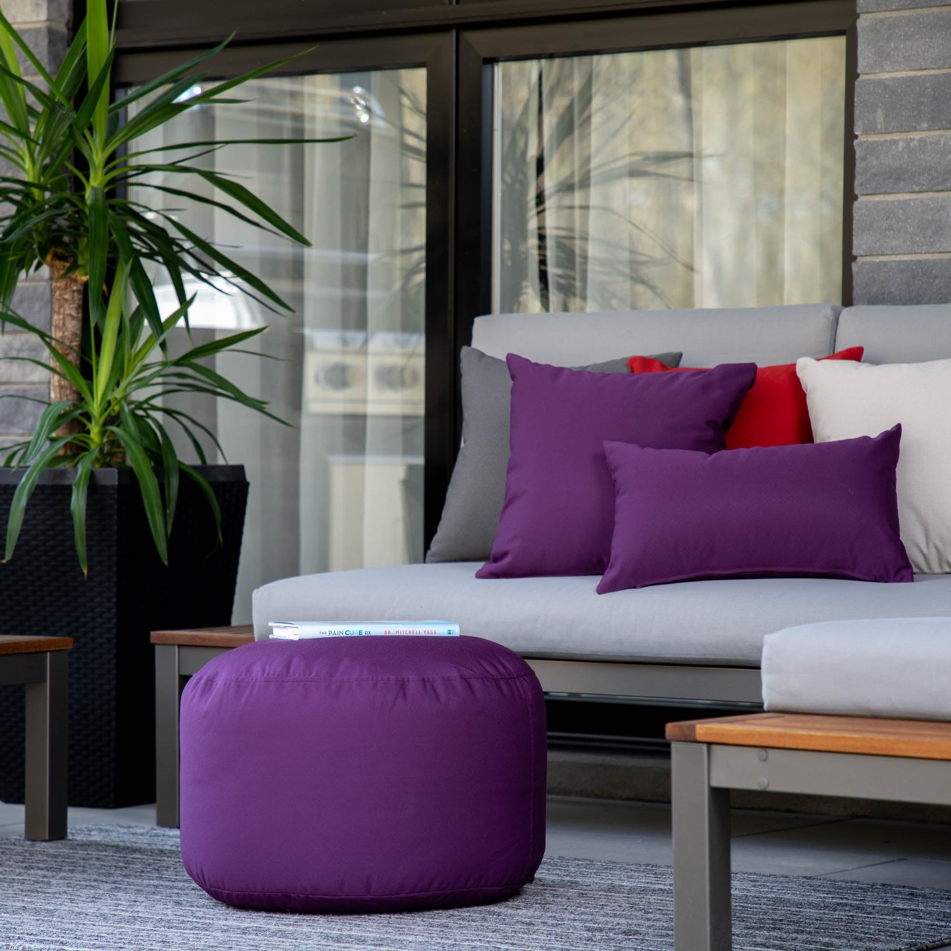 Outdoor seating area with a gray sofa, purple ottoman, and colorful cushions.