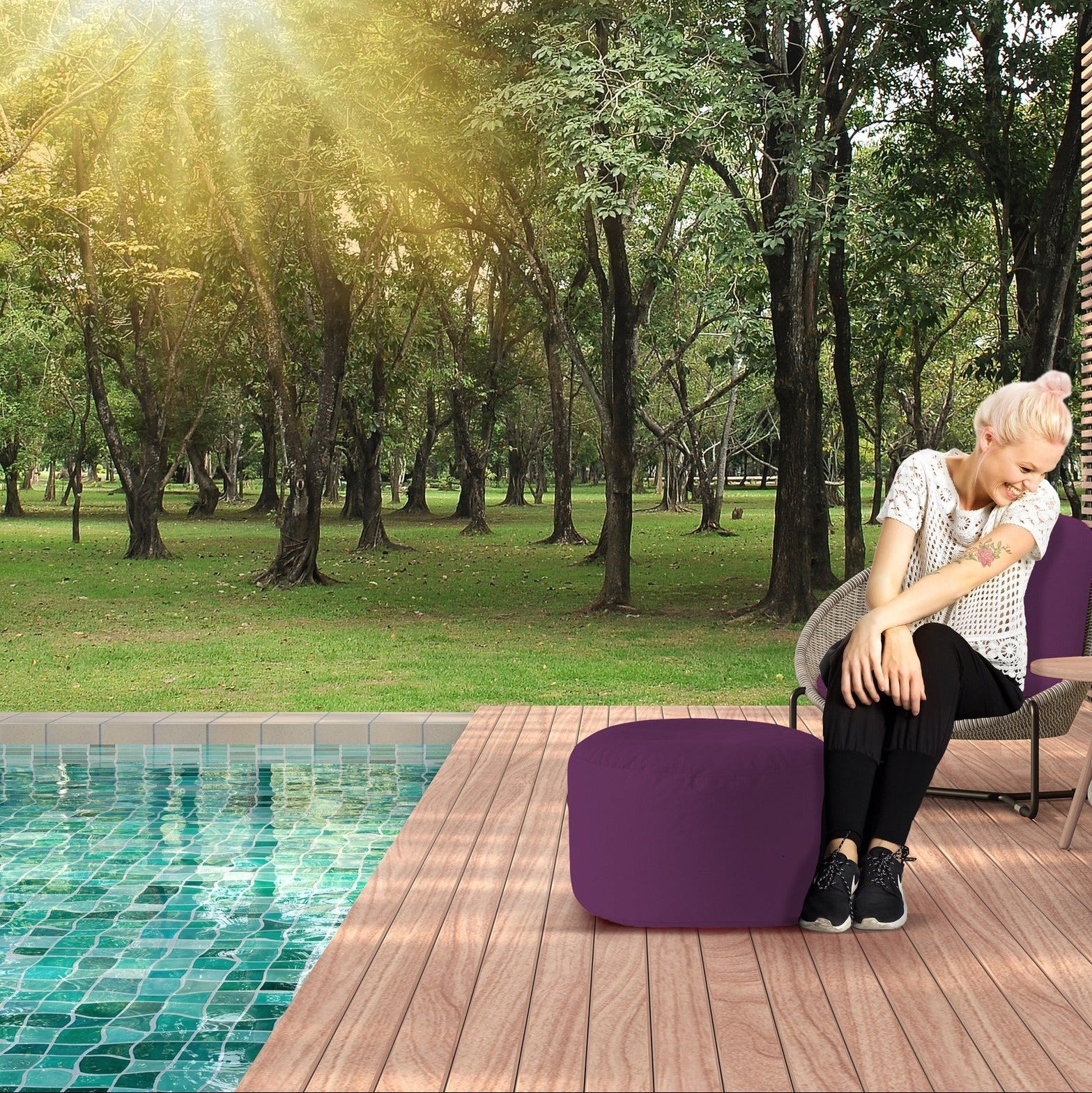Person sitting by a pool with a purple chair and sunlit trees in the background
