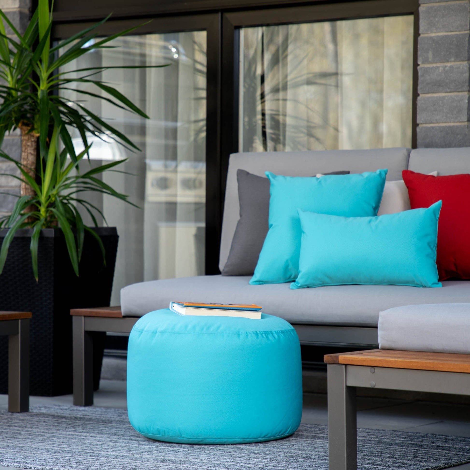 Outdoor seating area with a gray sofa, turquoise ottoman, and colorful cushions.