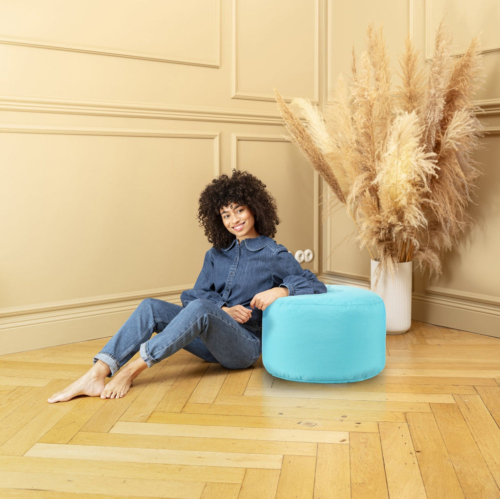 Woman sitting on a blue pouf in a room with beige walls and wooden floor.