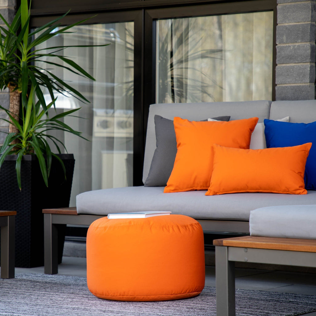 Outdoor seating area with a gray sofa, orange pouf, and colorful cushions.