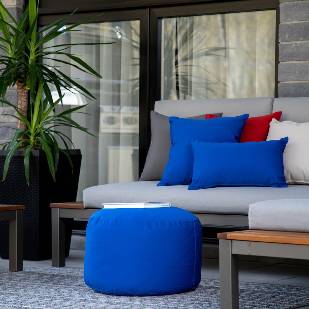 Outdoor seating area with a gray sofa, blue ottoman, and colorful pillows on a patio.