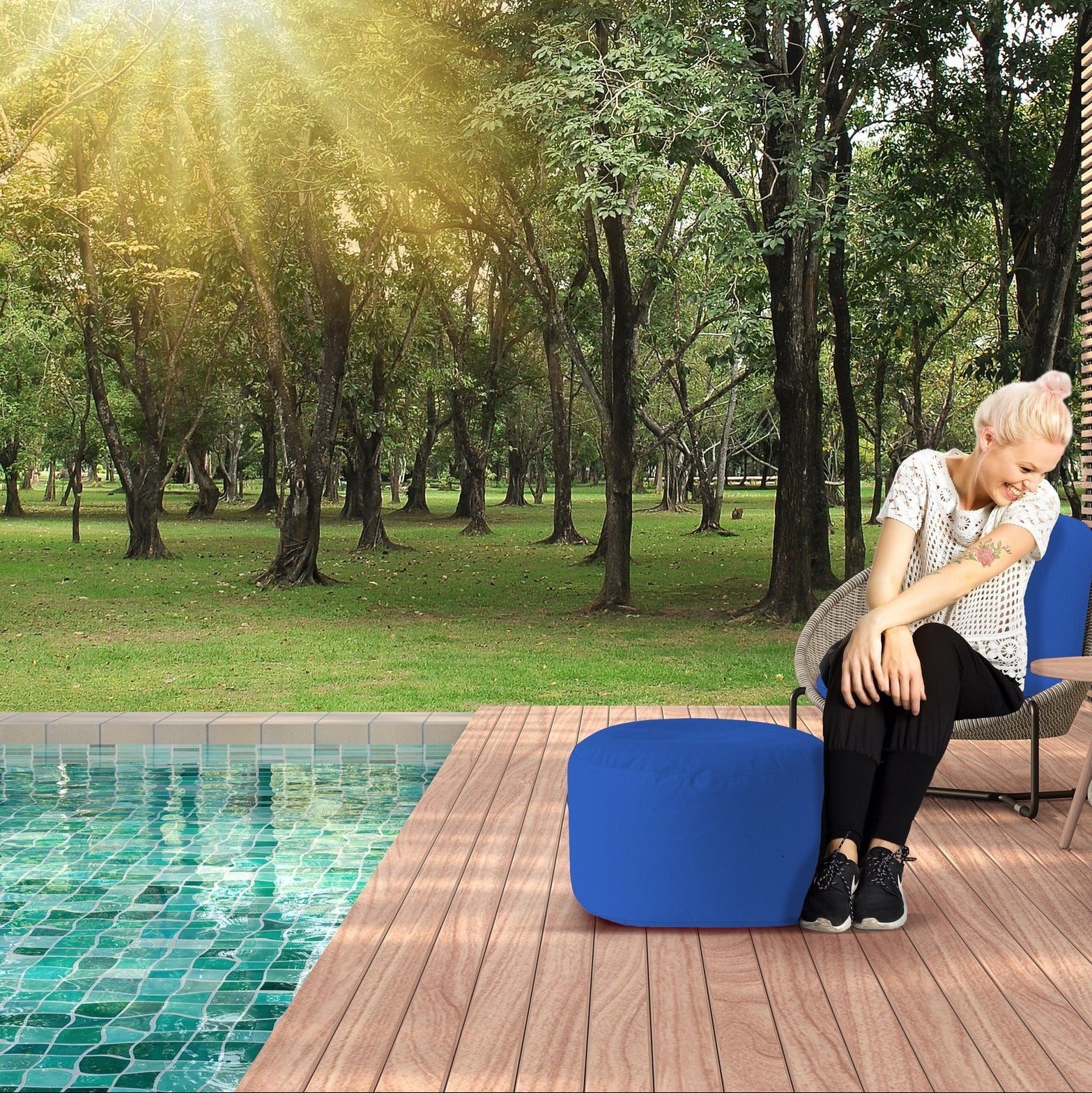 Woman sitting by a pool with a blue chair and sunlit trees in the background