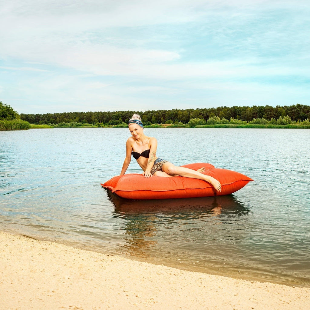 Woman sitting on a red inflatable raft in a lake with trees in the background