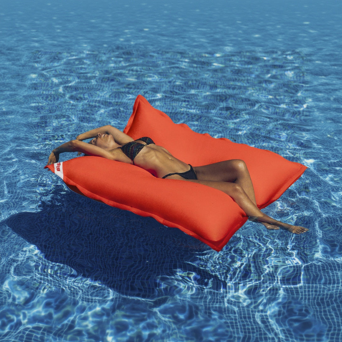 Person lying on a red inflatable lounger in a pool