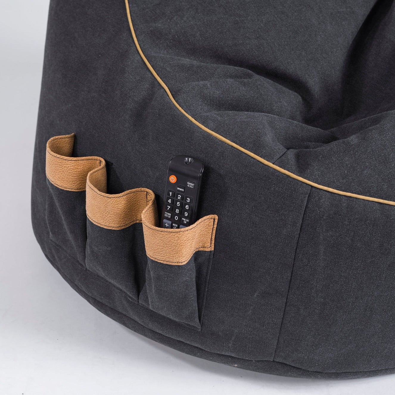 Dark gray bean bag with brown pockets and a remote control on a light gray background