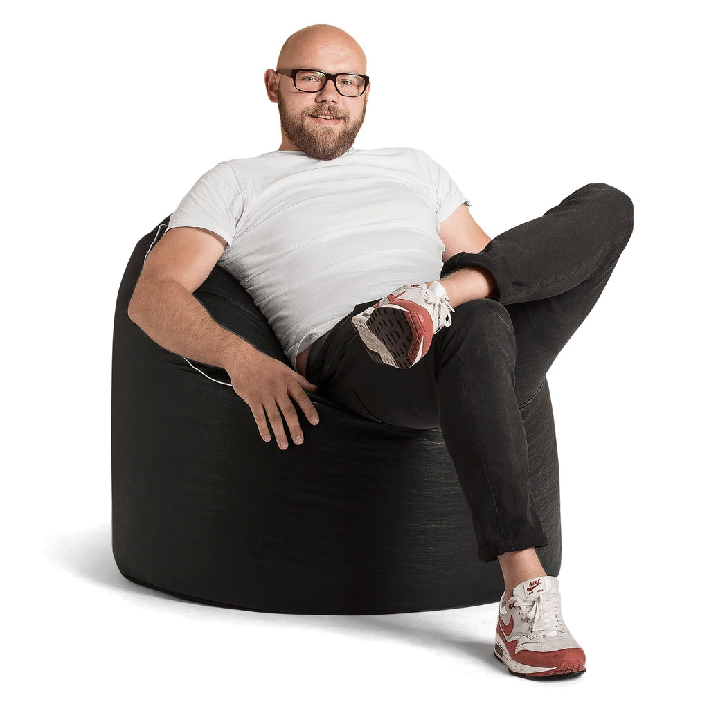 Man sitting on a black bean bag chair wearing glasses and casual clothing.