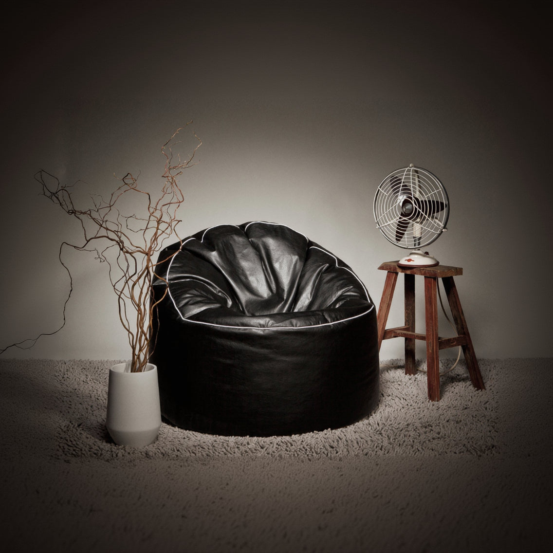 Black bean bag chair in a room with a vase, plant, and vintage-style fan.
