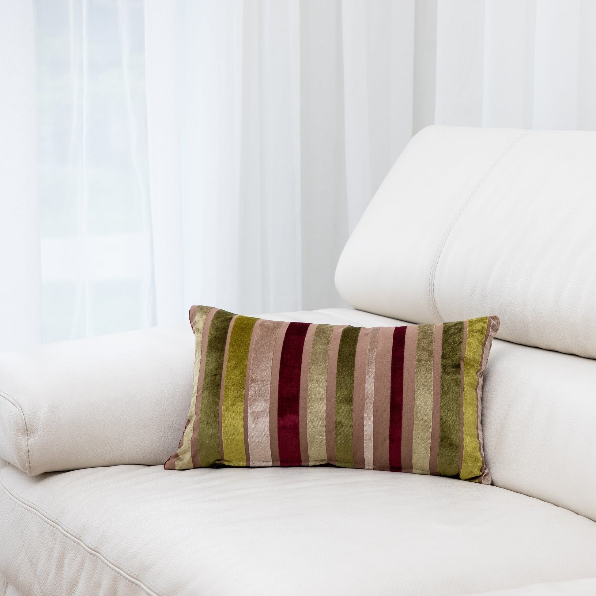 Striped pillow on a white couch with a white curtain background