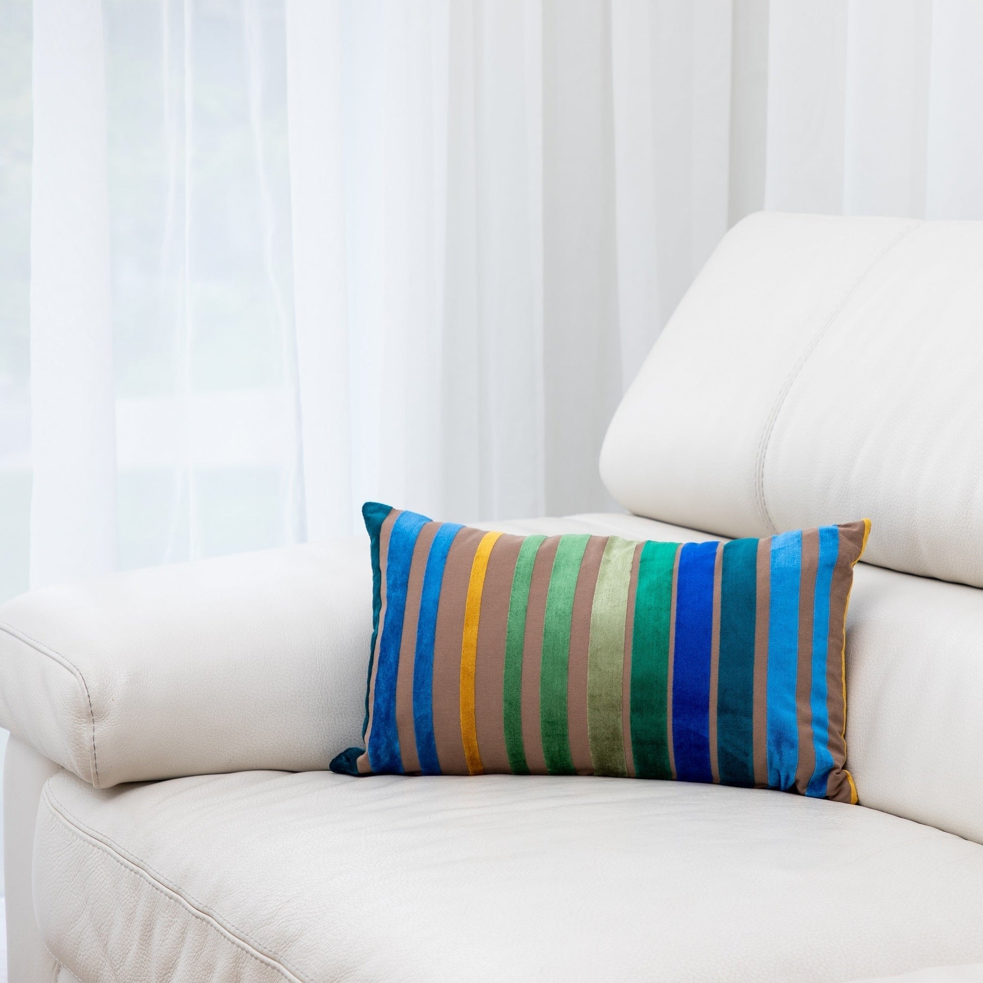Colorful striped pillow on a white sofa with a white curtain background