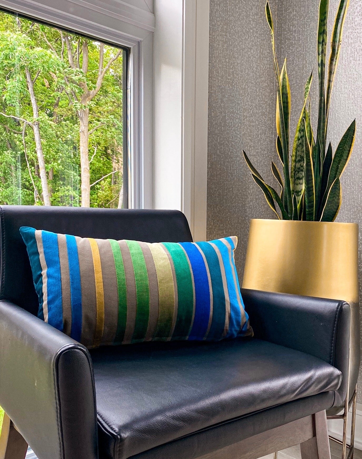 Striped pillow on a black chair with a plant in the background