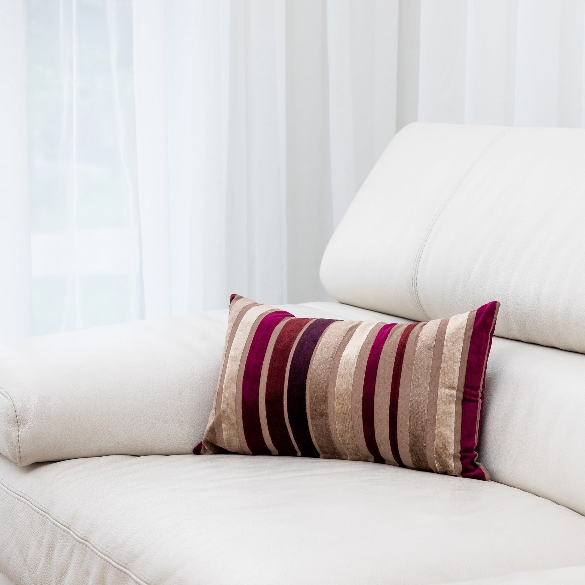 Striped pillow on a white sofa with a white curtain background