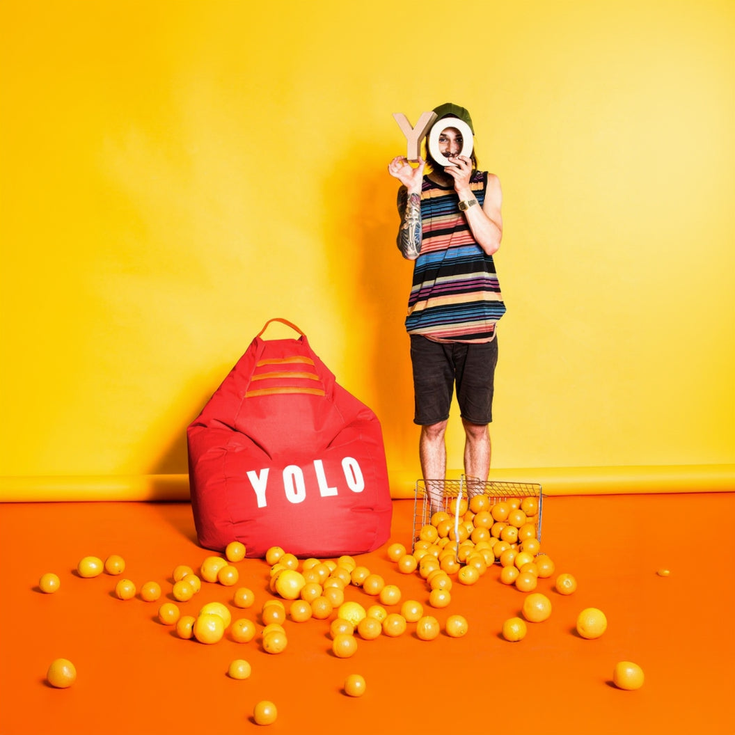 Person standing next to a red 'YOLO' bean bag with balls on an orange floor against a yellow wall.